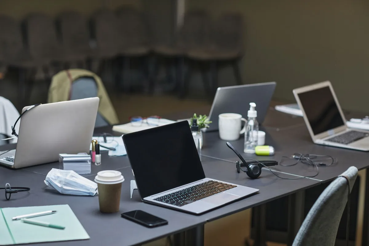A cluttered office desk setup featuring multiple laptops, coffee cup, and office supplies for a busy workday.