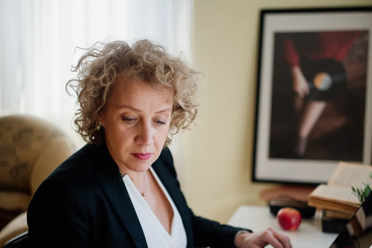 A person managing a laptop and documents at a desk in a bright office