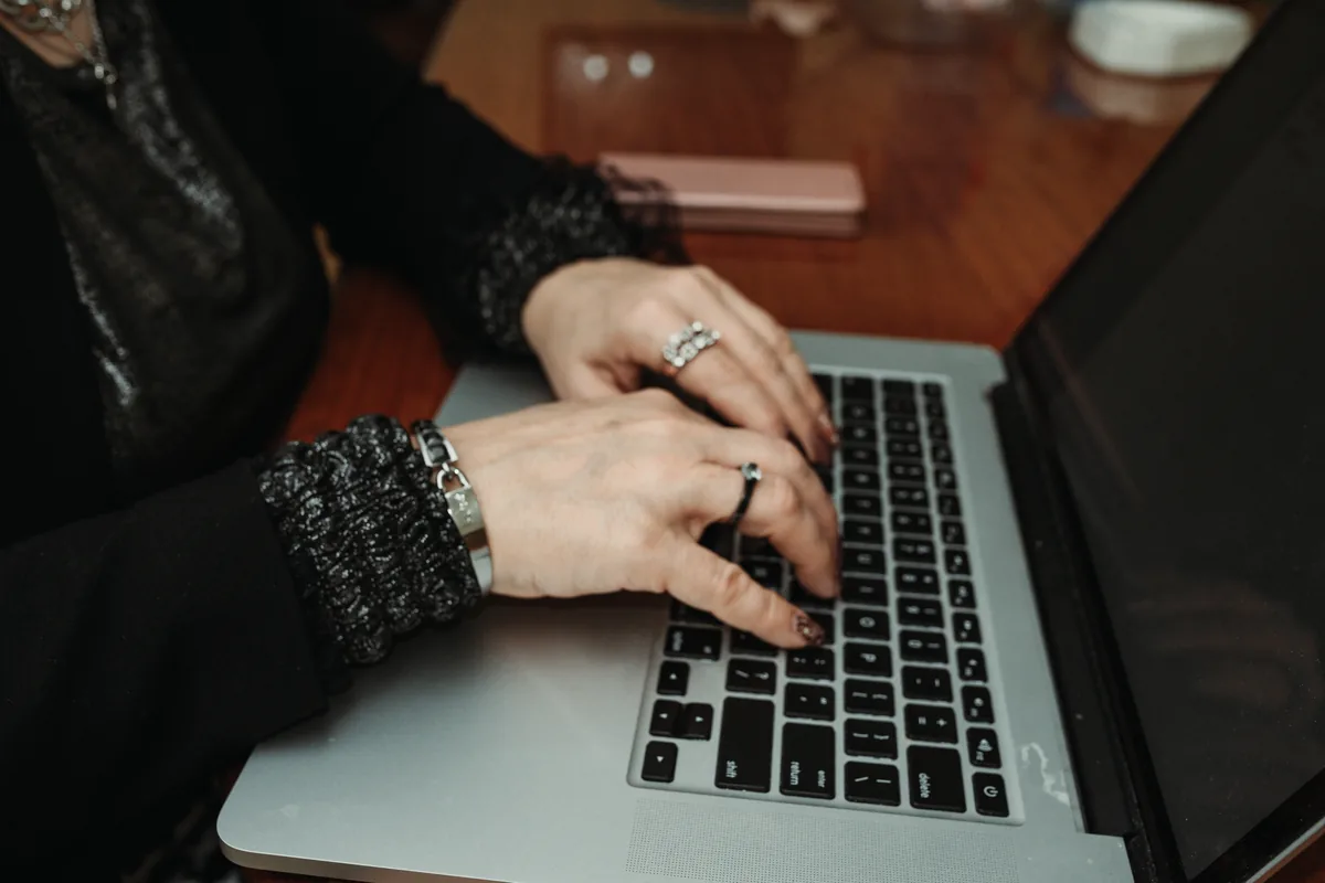 Close view of two hands typing on a laptop keyboard at a wooden table
